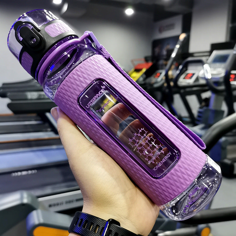 Purple water bottle with a textured design held in front of gym equipment.
