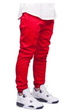 Red pants worn with a white top and white sneakers on a white background