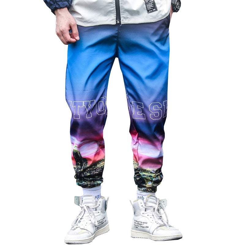 Colorful tie-dye jogger pants with a landscape design worn by a person on a white background.