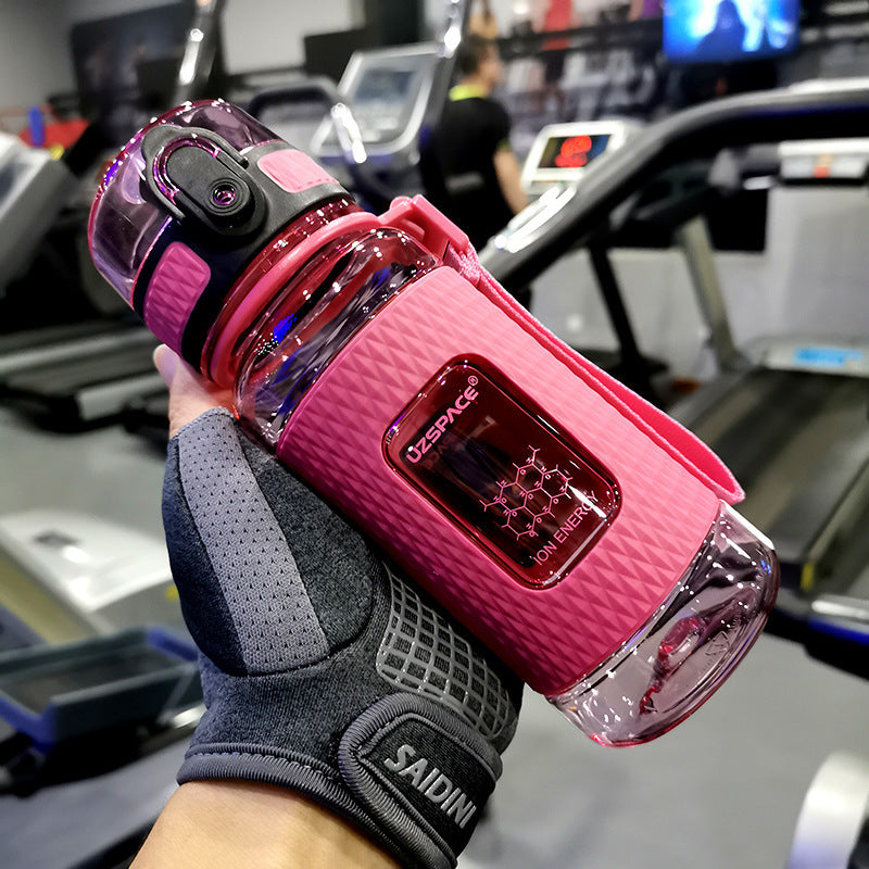 Pink water bottle with clear design held by a gloved hand in a gym setting