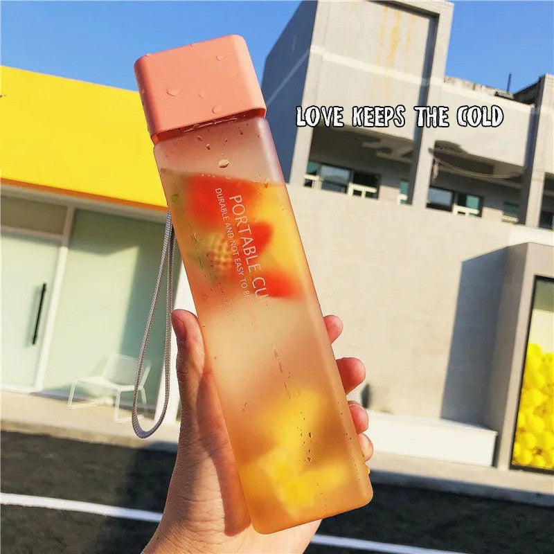 Hand holding a gradient water bottle with 'LOVE KEEPS THE COLD' text against a building background