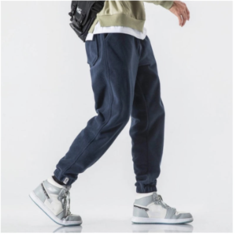 Person wearing navy jogger pants and gray sneakers on a white background
