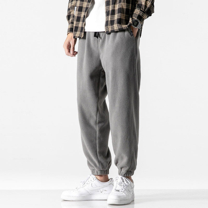 Person wearing gray sweatpants with a plaid shirt and white sneakers on a white background