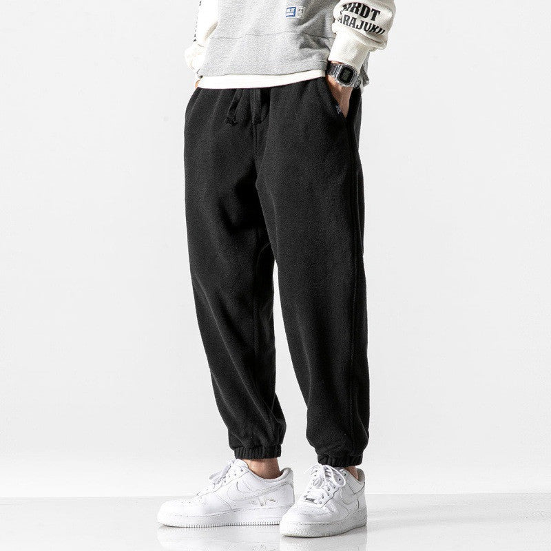 Person wearing black jogger pants and white sneakers on a light gray background
