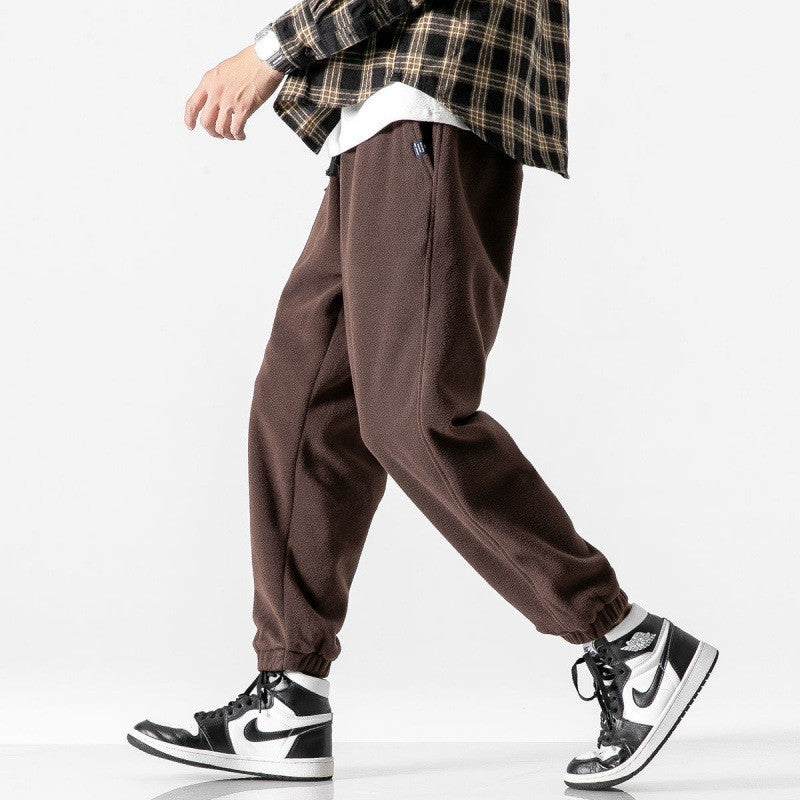 Person wearing brown baggy pants with a plaid shirt and black and white sneakers on a white background
