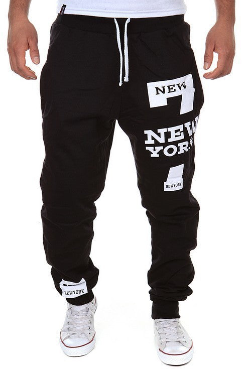 Black jogger pants with 'New York' text worn by a person on a white background