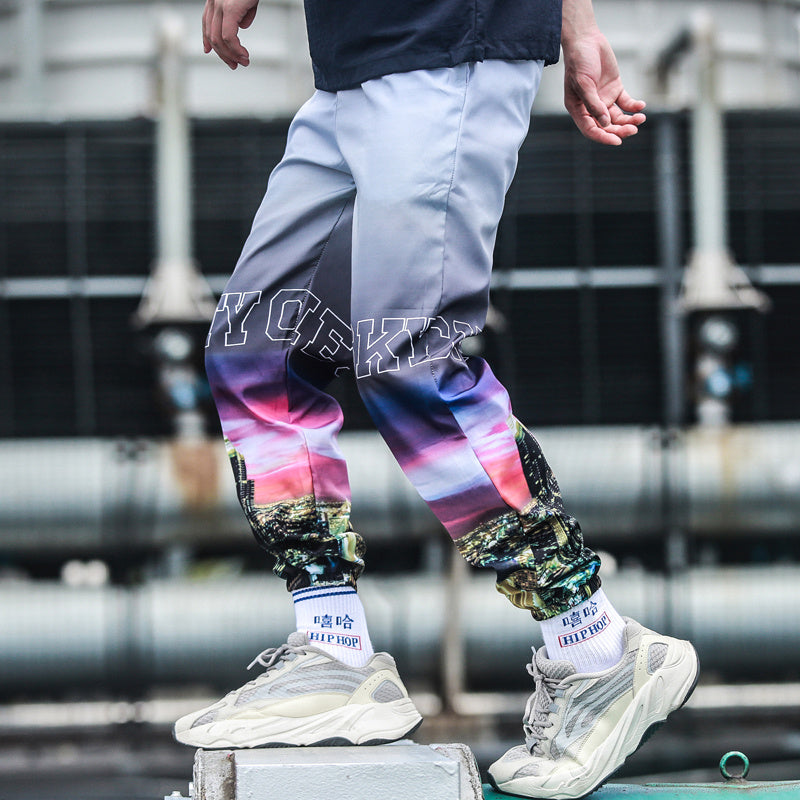 Person wearing colorful pants with a tie-dye pattern and text, standing on a concrete surface.