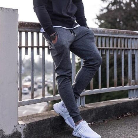 Person wearing dark hoodie, gray jogger pants, and white sneakers on a railing.