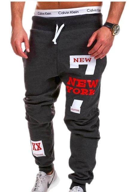 Dark gray sweatpants with 'New York' text and patches, worn by a person.