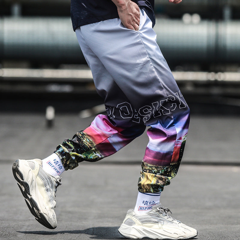 Person wearing colorful pants with text and white sneakers on a blurred background