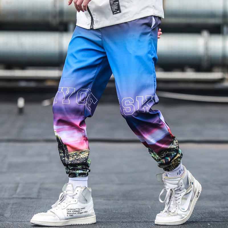 Person wearing gradient pants with colorful design and white sneakers on a blurred background