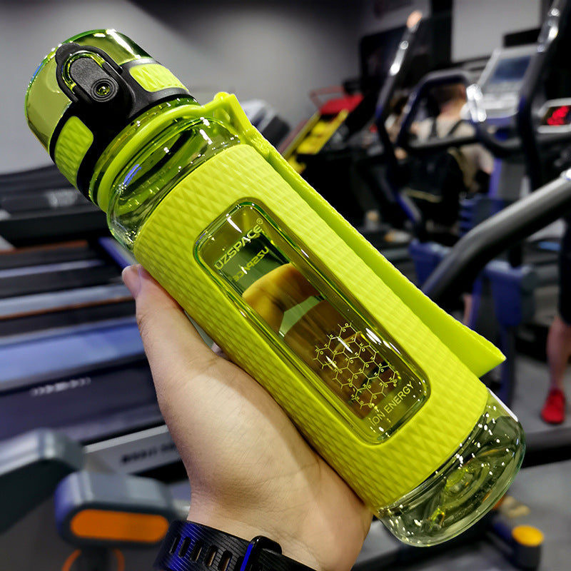 Hand holding a green water bottle with a gym in the background