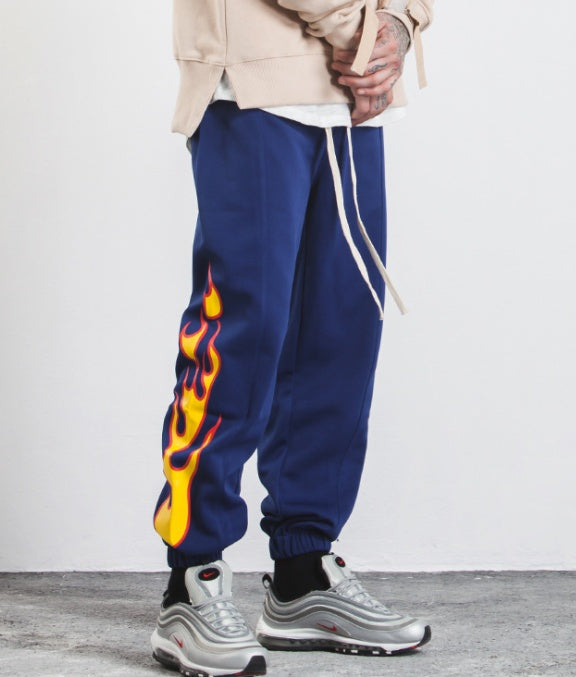 Person wearing blue sweatpants with flame design and gray sneakers on a white background