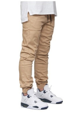 Beige pants worn with a white shirt and white sneakers on a white background