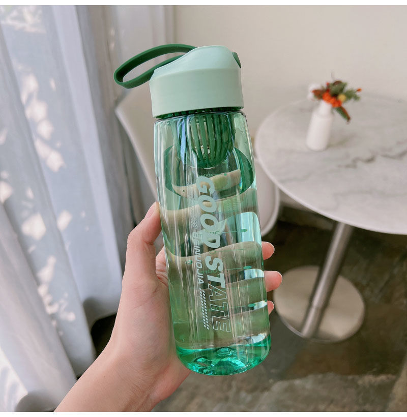 Green water bottle held by a hand with a blurred indoor background