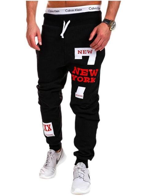 Black jogger pants with 'New York' text and patches on a white background