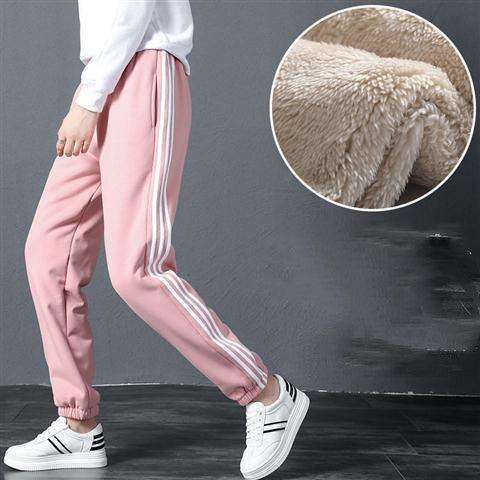 Pink tracksuit pants with white stripes and white sneakers on a gray background