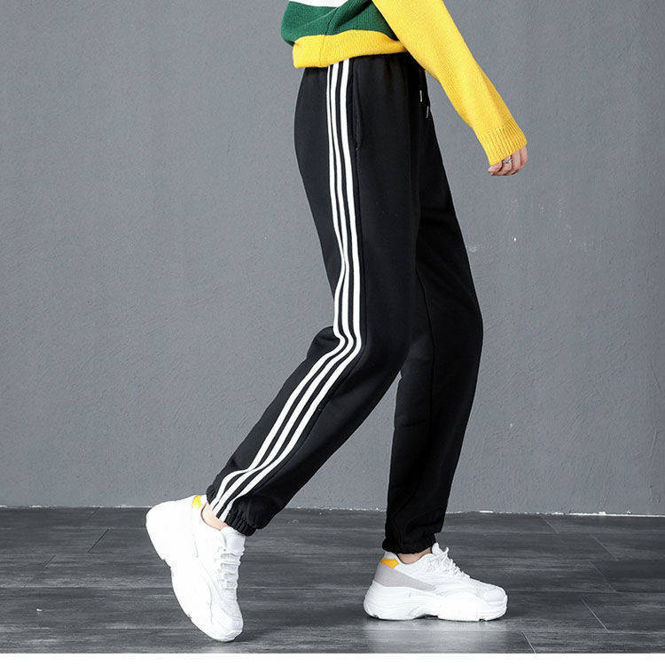 Black track pants with white stripes worn by a person against a gray background