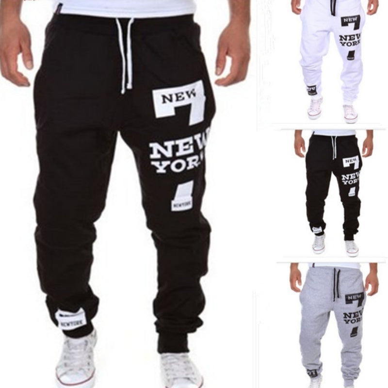 Black jogger pants with 'New York' text and white sneakers on a white background.