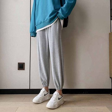 Person wearing a blue sweatshirt, gray jogger pants, and white sneakers in a minimal indoor setting.