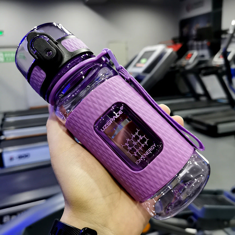 Purple sports bottle with a digital display held in front of a treadmill.