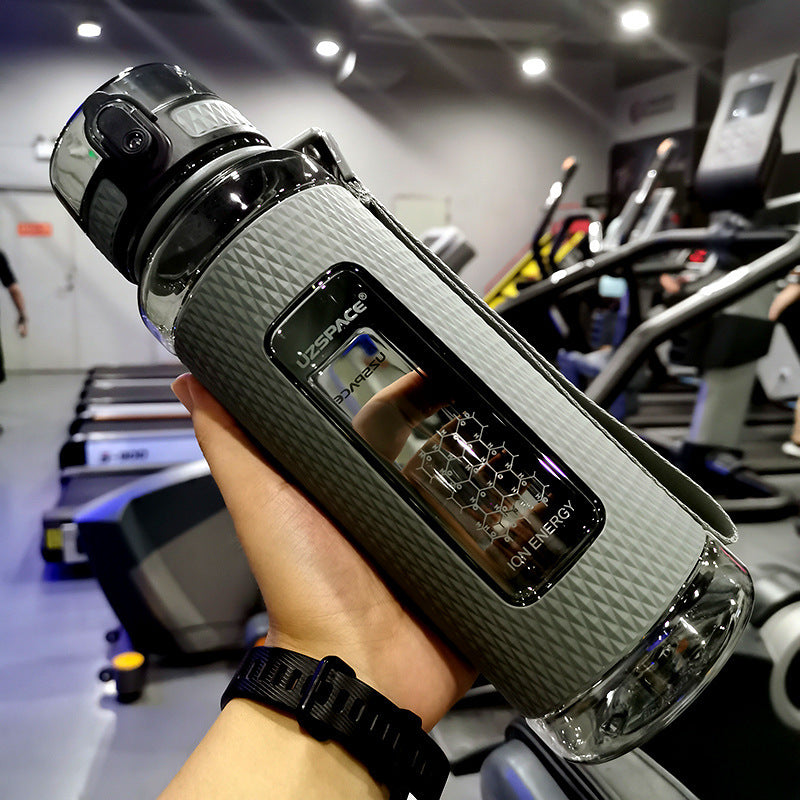 Person holding a textured water bottle with digital display in a gym setting
