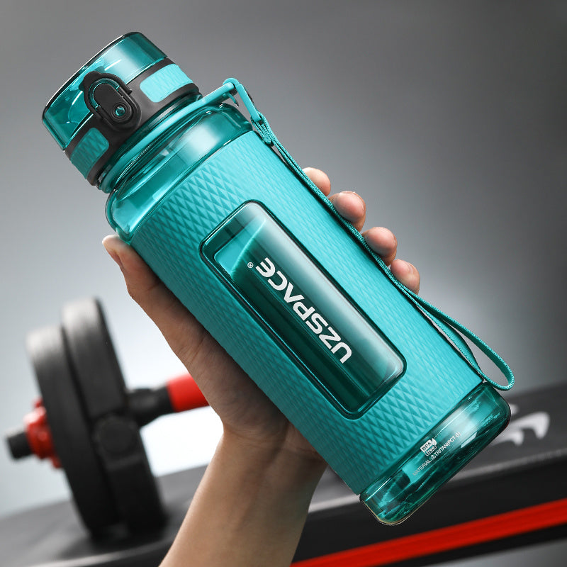 Turquoise water bottle with 'UZSPACE' branding held by a hand, with a blurred gym background.