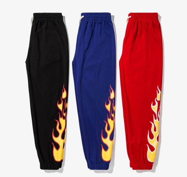 Three pairs of pants in black, blue, and red with flame designs on a white background.