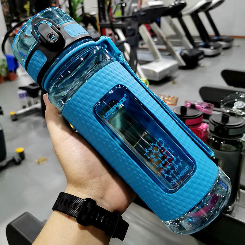 Blue water bottle with a textured grip held in a hand, gym equipment in the background