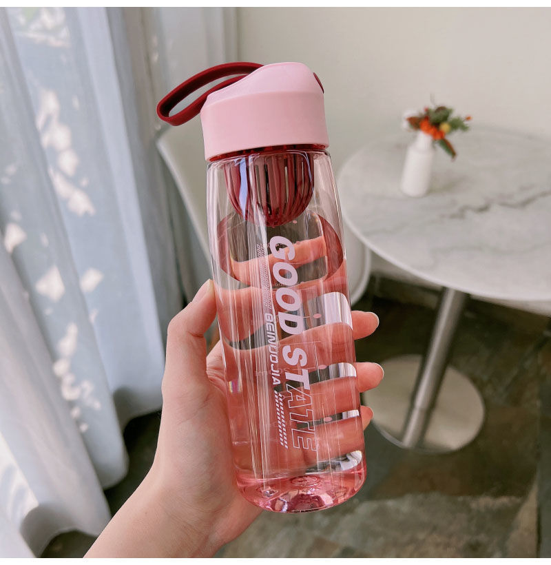 Hand holding a pink water bottle with a clear design in a home setting