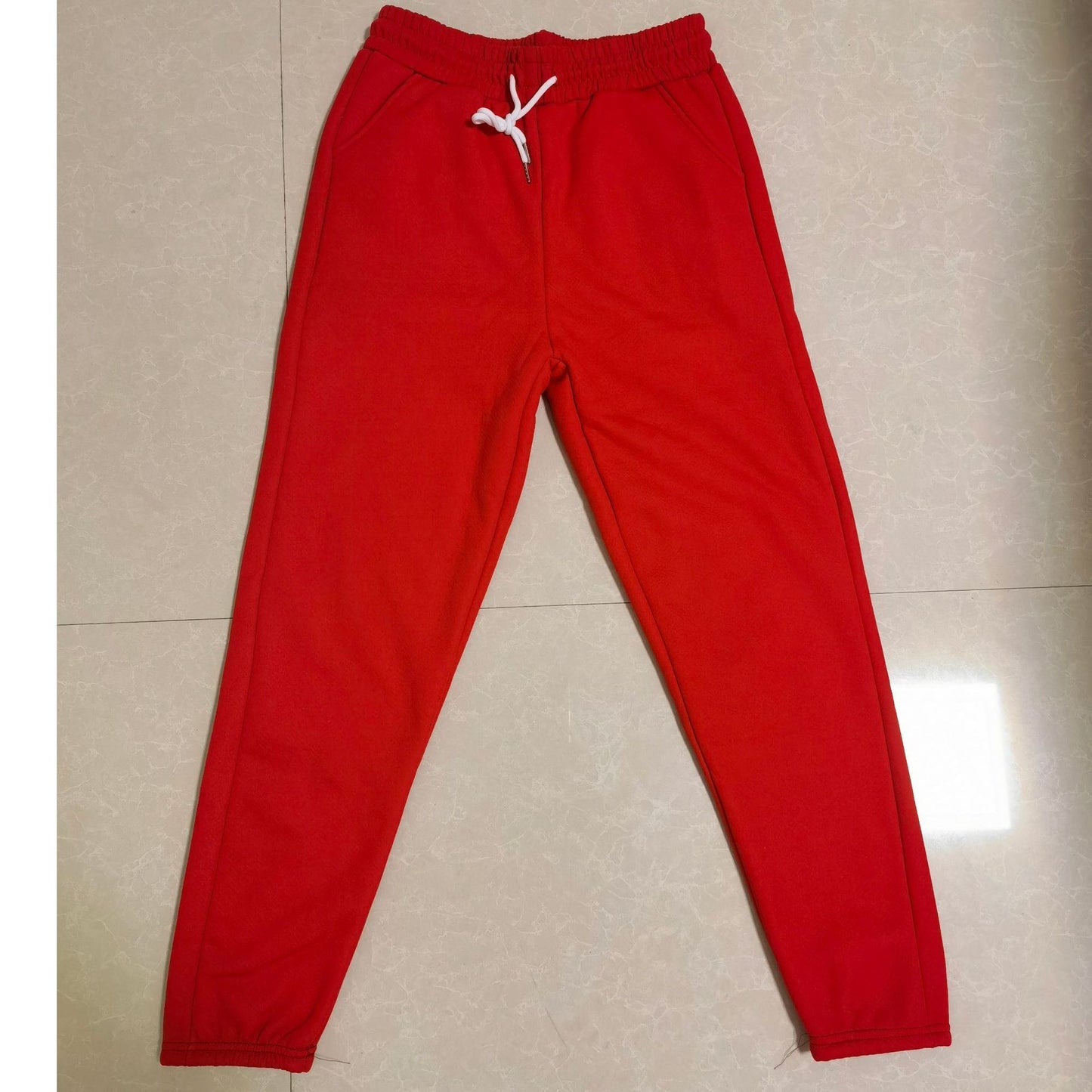 Red sweatpants with a white drawstring on a beige floor.
